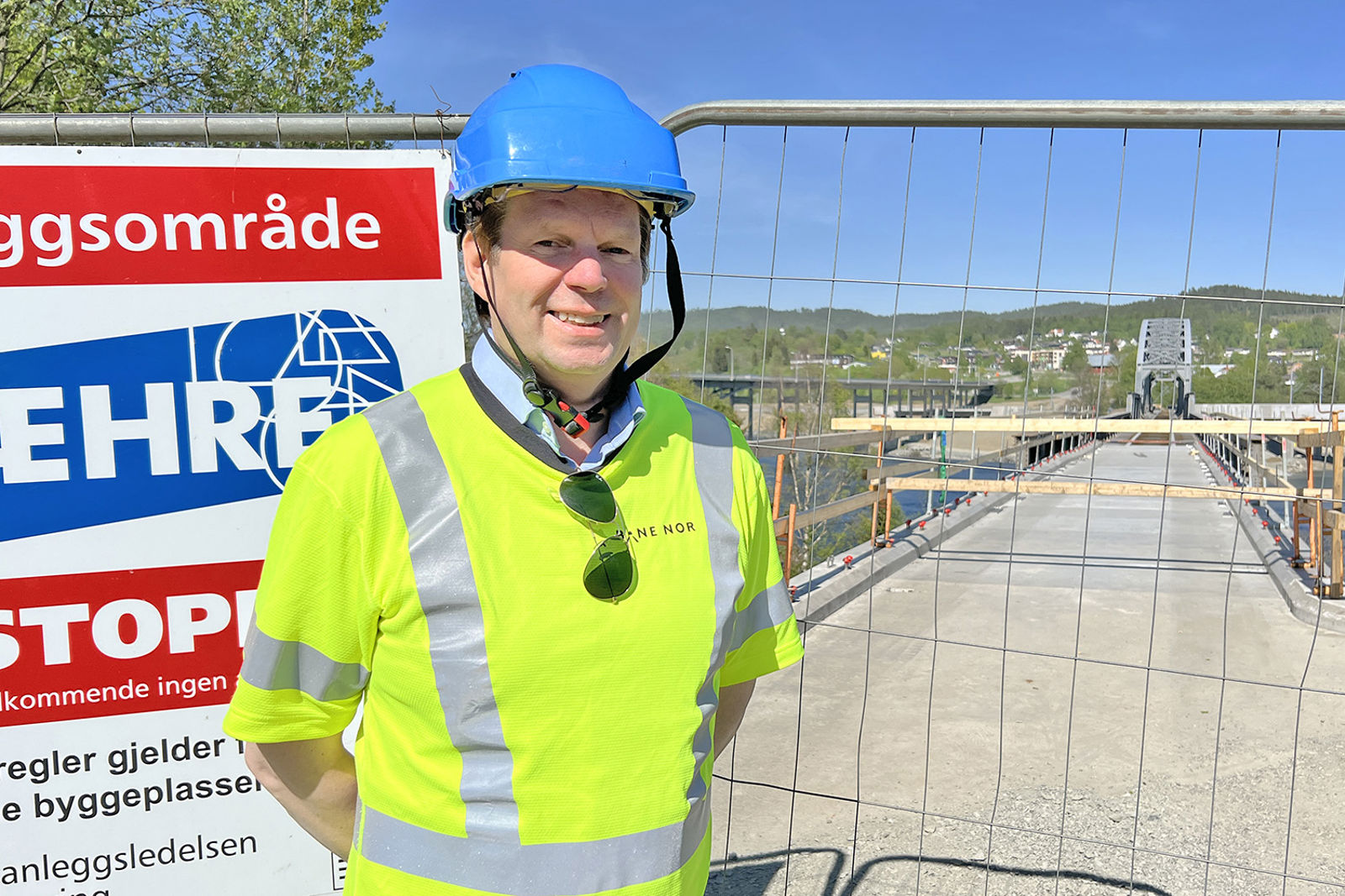 Prosjektlederen i vernetøy og hjelm med anleggsgjerdet og brua i bakgrunnen.