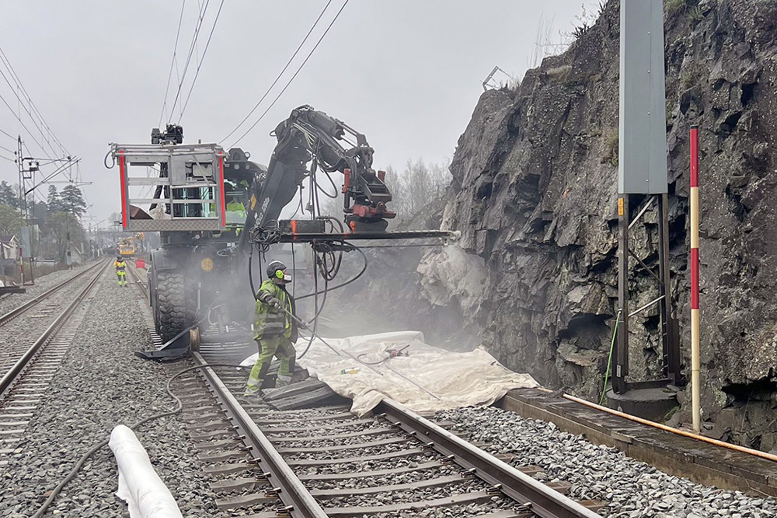 En skinnegående arbeidsmaskin borer bolter inn i fjellet, mann i verneutstyr foran.