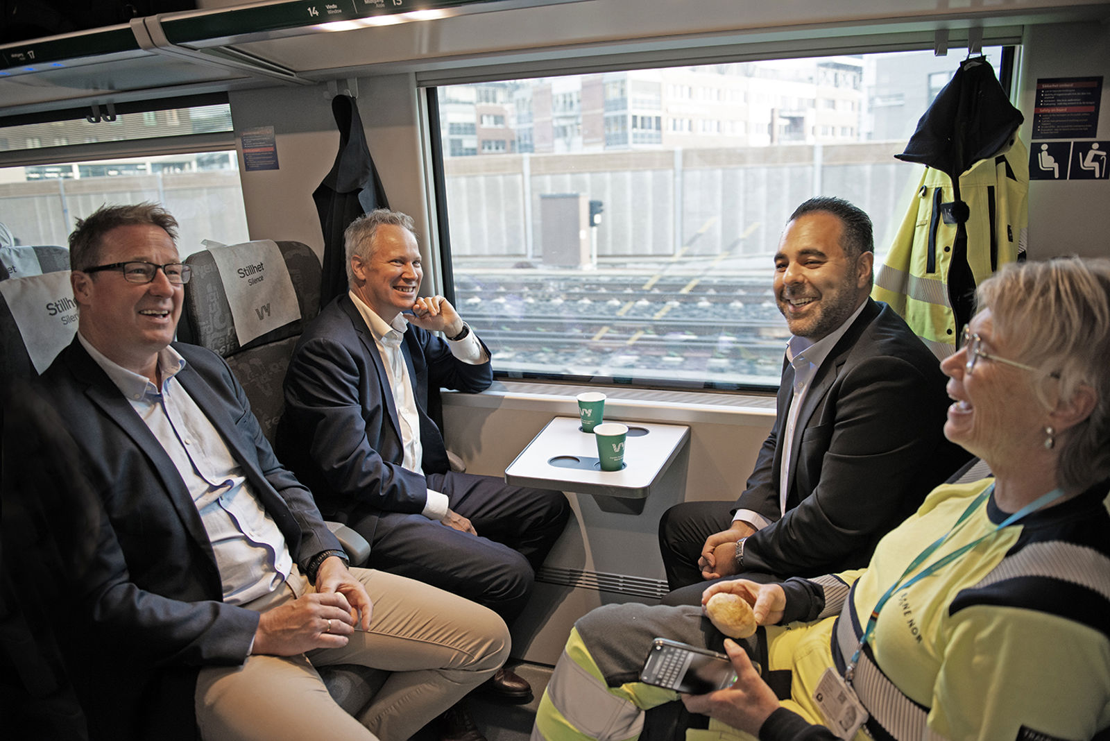 Svært bilde sit dei fire i togkupeen med kaffe og bollar.