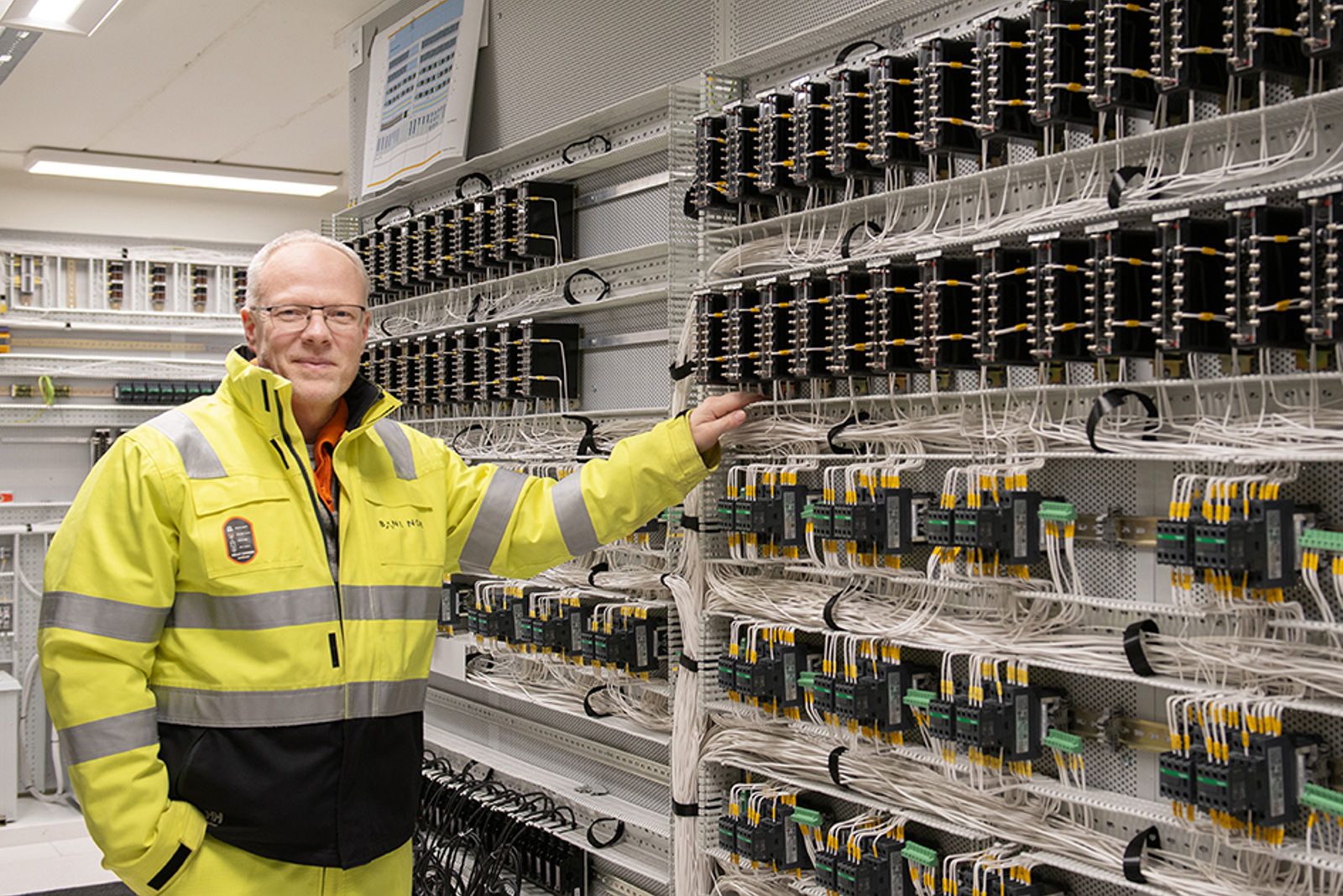 Bilde av mann i vernetøy i et rom med veldig mange ledninger.