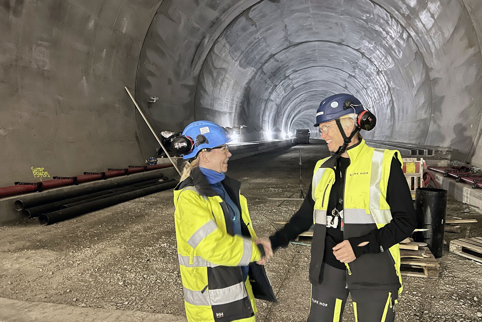 To kvinner kledt i verneutstyr smiler og utveksler håndtrykk.