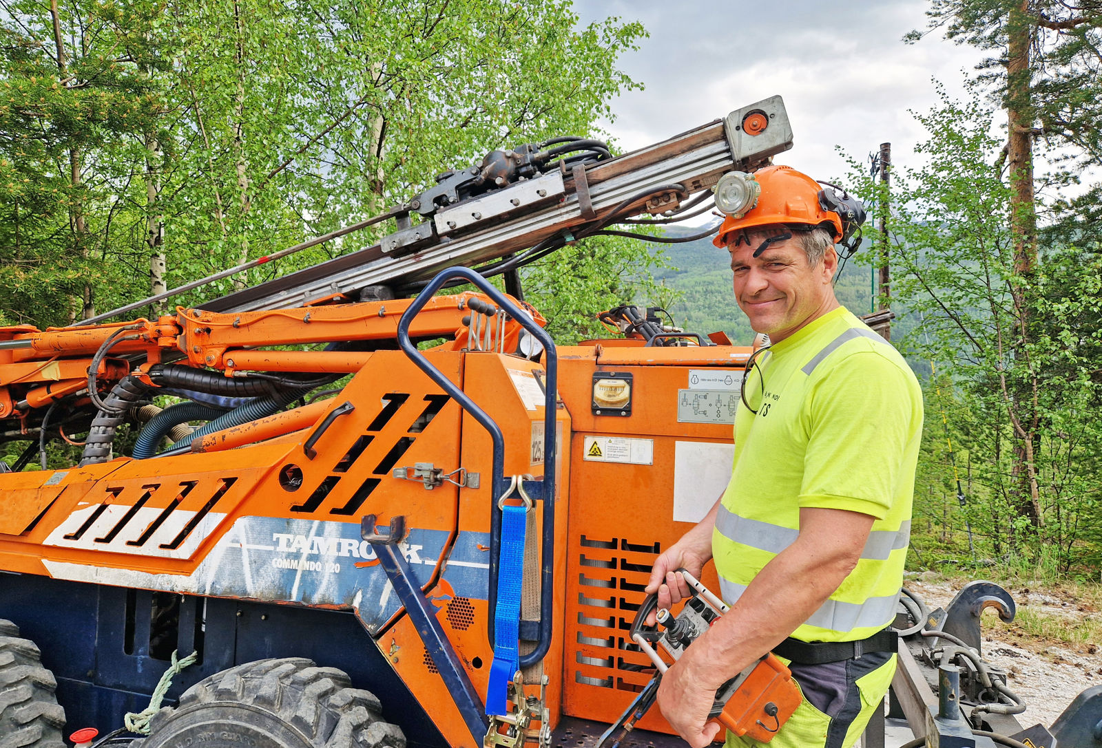 En mann i vernetøy står foran en oransje anleggsmaskin, som er en borerigg.