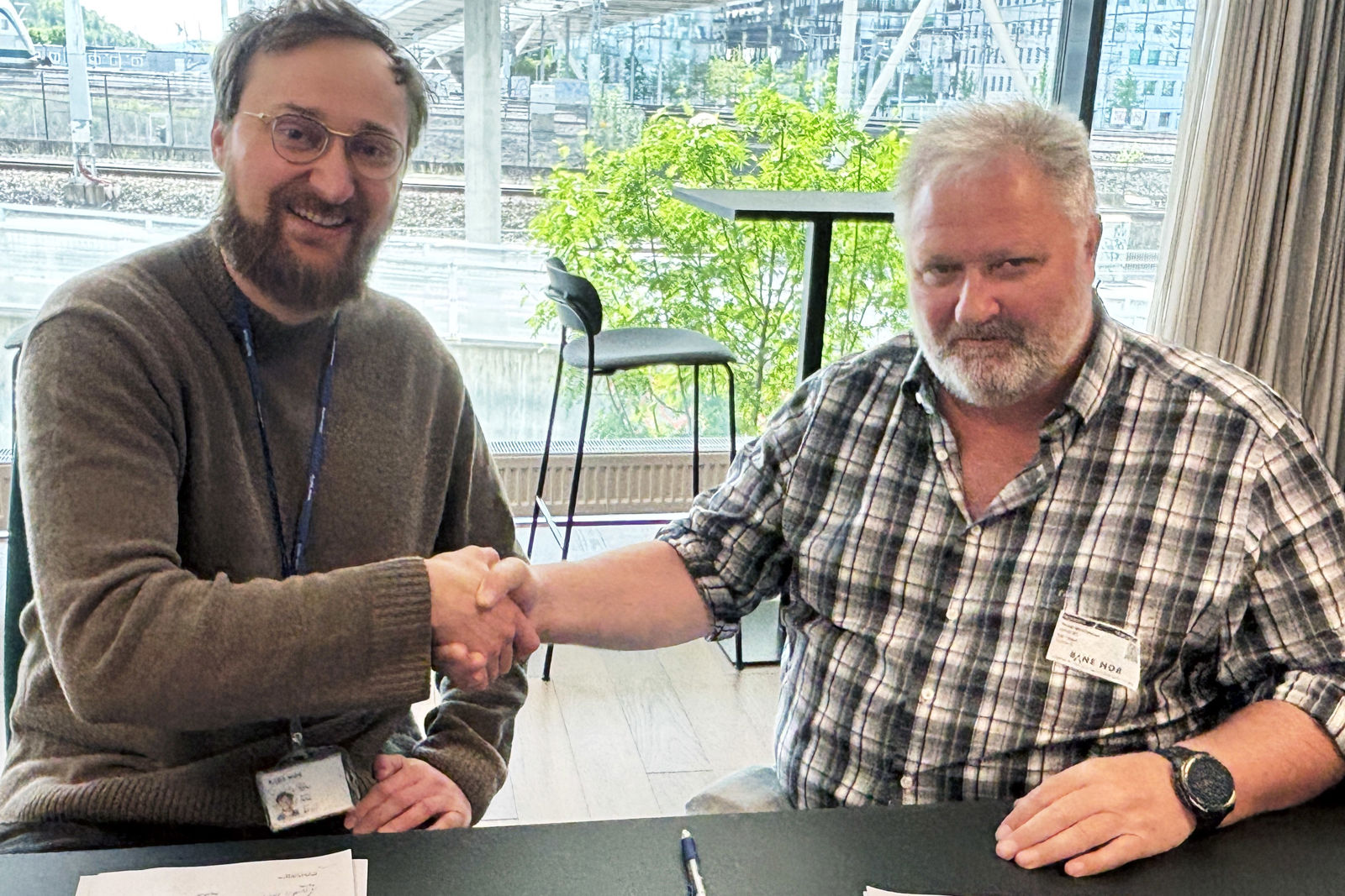 To menn håndhilser, smiler og ser i kamera.