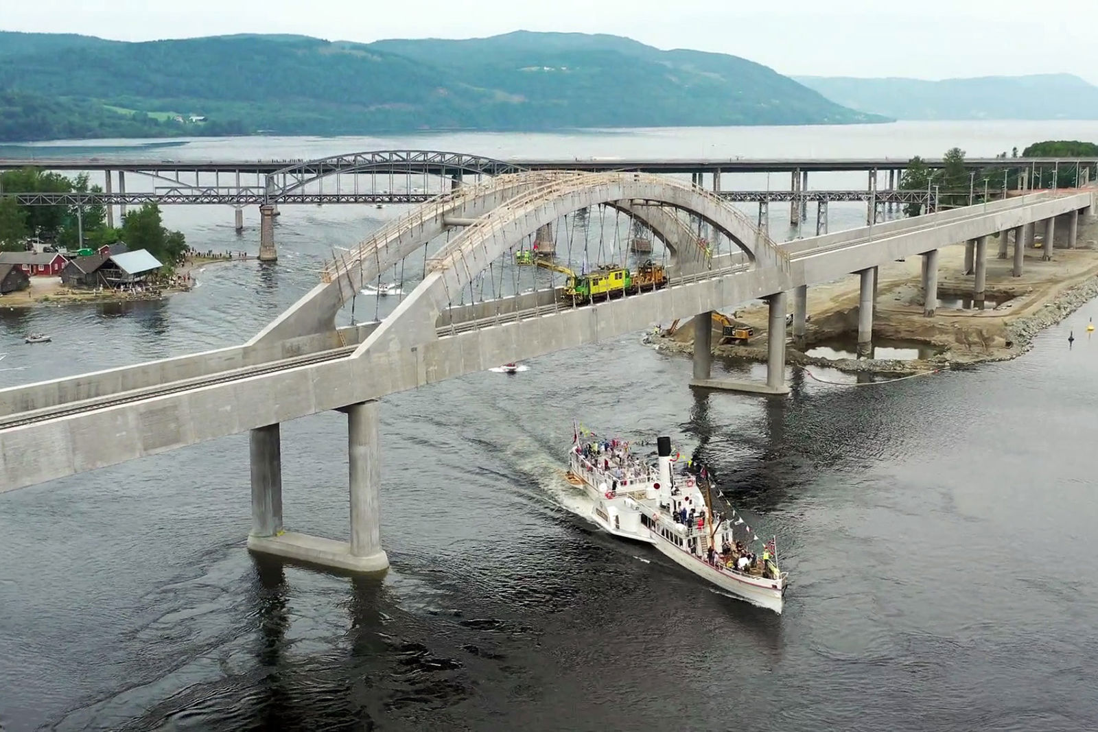 Skibladner under den store buen på Minnevika bru. Et arbeidstog hilser båten oppe på brua.