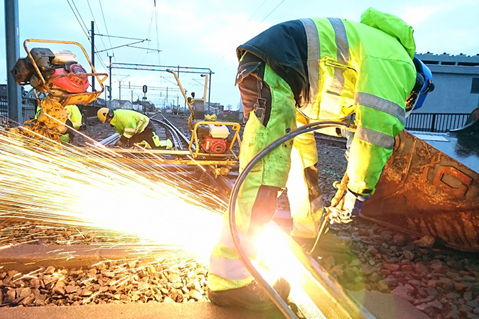 Bilde av folk i arbeidsklær som sveiser i skinnegangen så gnistene fyker.