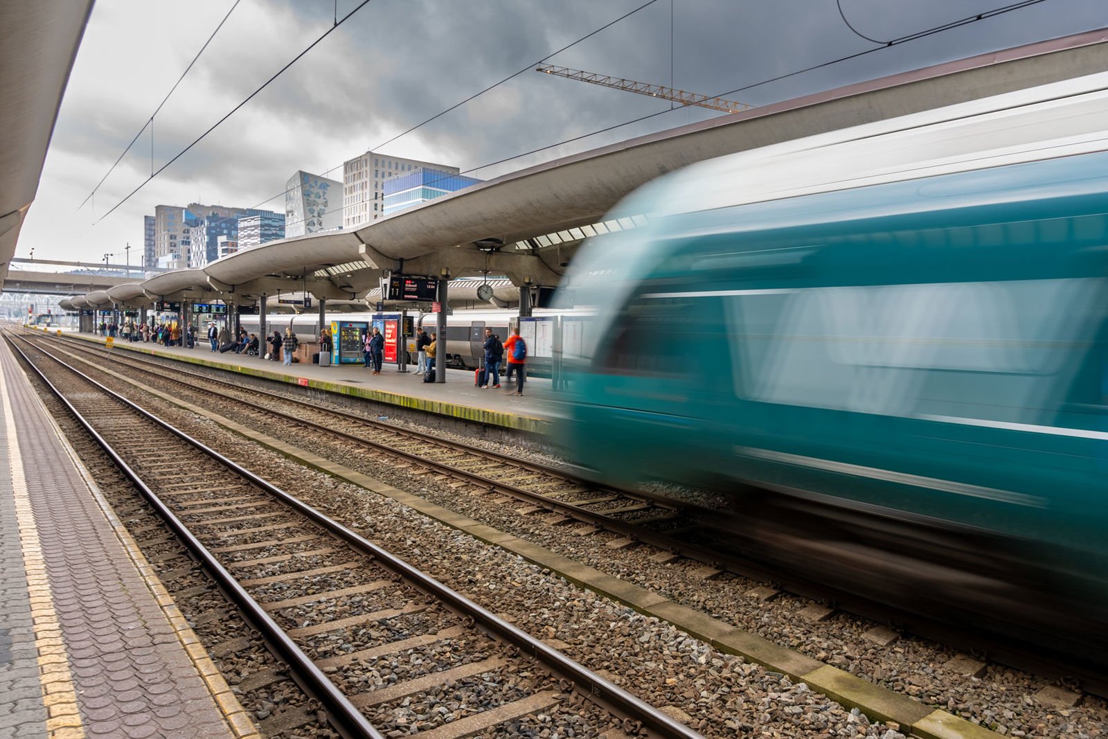 Et grønt Vy-tog kjører inn til plattform på Oslo S. Passasjerer og andre tog i bakgrunnen.